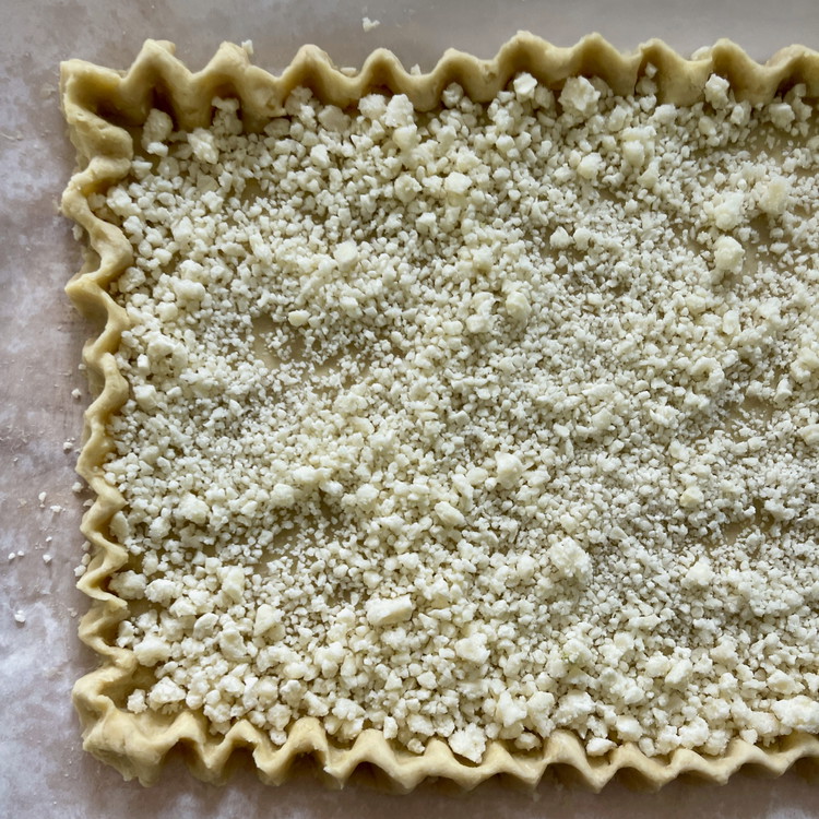 Image of Move the dough and paper onto the baking tray and spread the parmesan to cover the bottom of the tart shell.